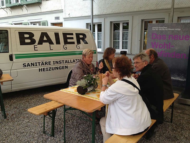 Menschen unterhalten sich an Picknicktischen neben einem BAIER-LKW und einem Schaufenster im Freien.