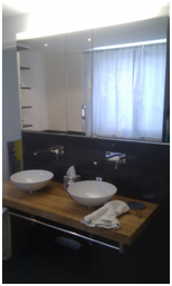 Modernes Badezimmer mit Doppelwaschbecken, Holzablage und Fenster mit transparenten Vorhängen.