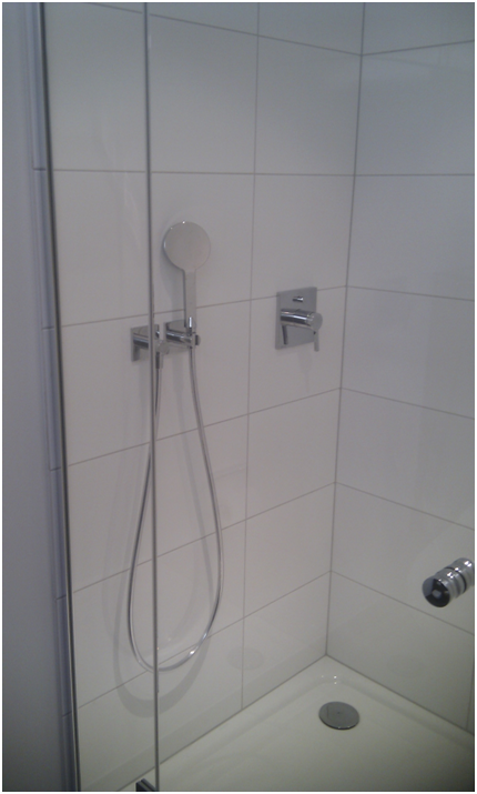 Geflieste Duschecke mit Handbrause, Brauseschlauch, Haltegriffen und Abfluss