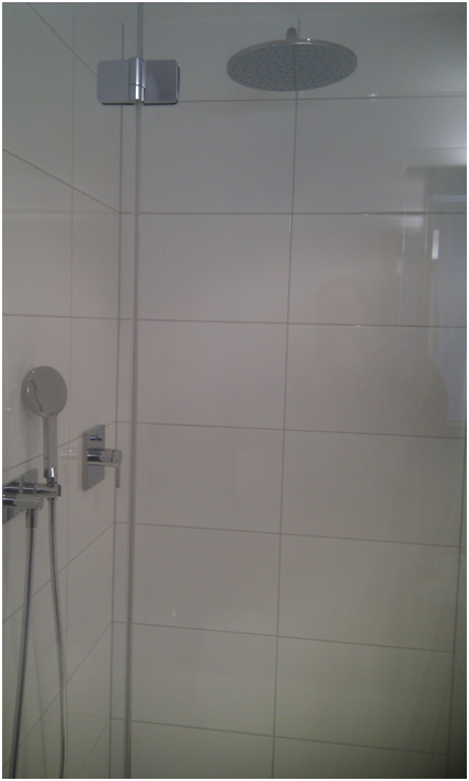 Duschkabine mit Glastür, weiss gefliesten Wänden, Duschkopf und Handbrause.