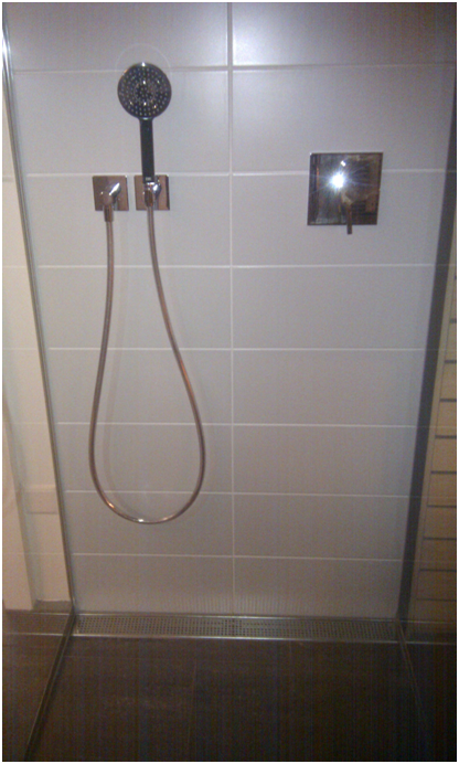Duschkabine mit wandmontiertem Duschkopf, Schlauch und Armaturen an gefliester Wand.