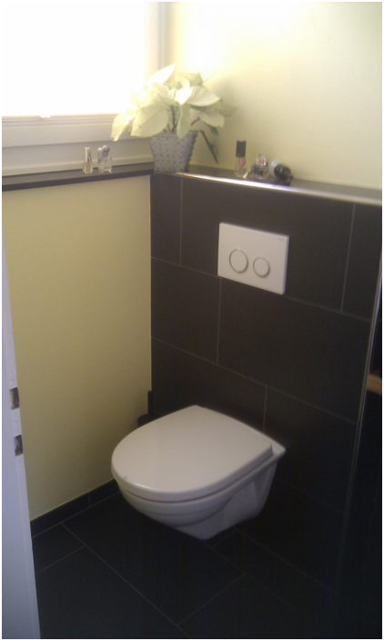 Kleines Badezimmer mit wandhängender Toilette, dunkel gefliester Wand und einem weissen Blumenarrangement auf dem Sims.