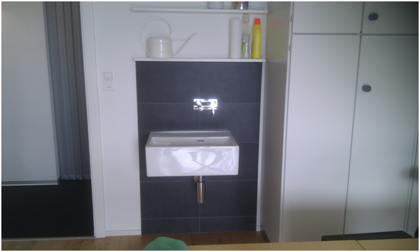 Küchenschrank mit kleinem Spülbecken, weissen Arbeitsplatten und dunkler Holzoberfläche.