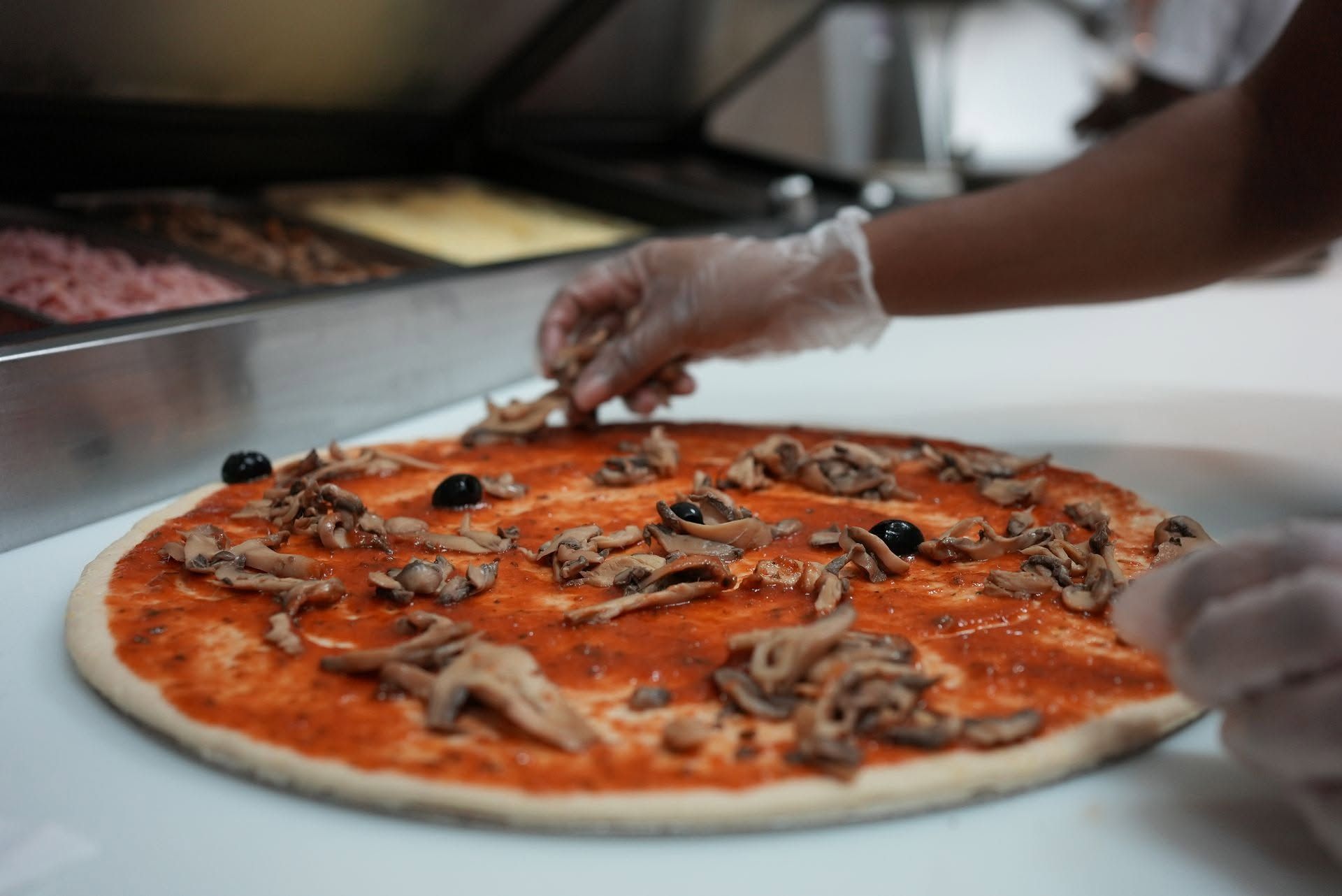 Des mains garnissent une pizza au fromage, aux champignons et aux olives sur un plan de travail.