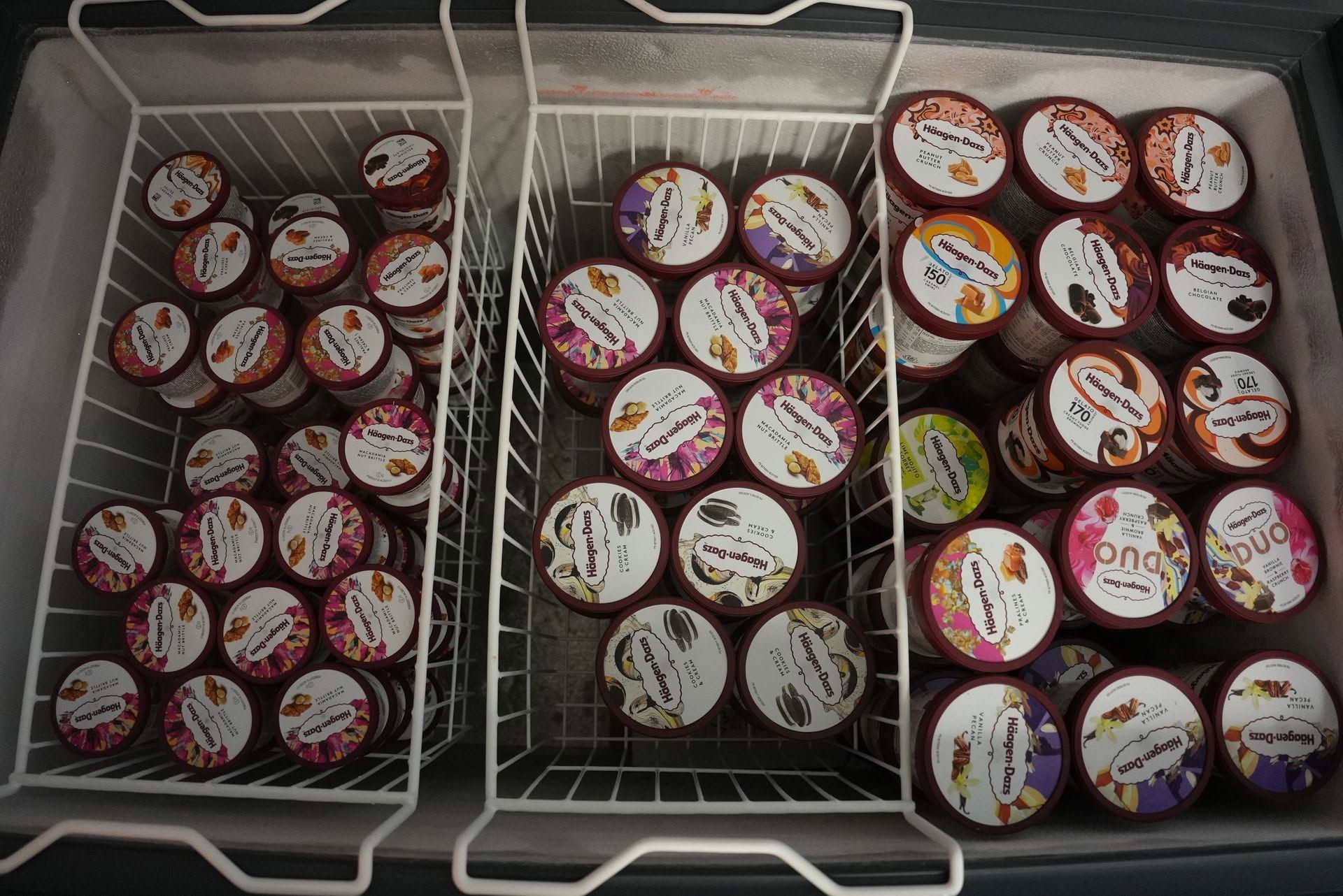 Réfrigérateur ouvert avec des rangées de petits pots à dessert assortis, répartis en trois compartiments, principalement avec des étiquettes rouges, blanches et violettes.