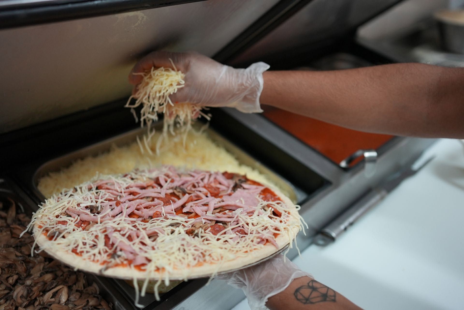 Déposer à la main du fromage râpé sur une pizza avant la cuisson