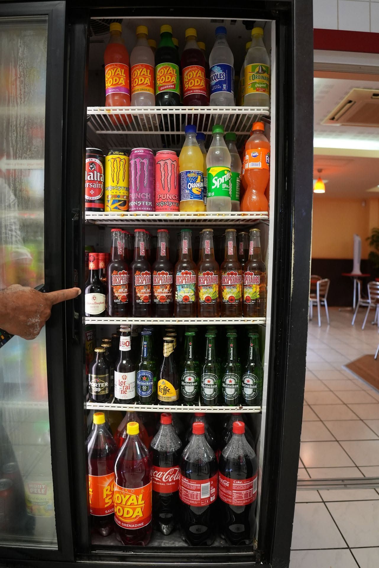 Vitrine réfrigérée ouverte remplie de bouteilles et de canettes de sodas et de jus assortis, une main ouvrant la porte.