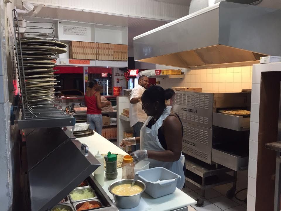 Cuisine professionnelle animée avec deux employés préparant des aliments près d'un comptoir et d'un four en acier inoxydable