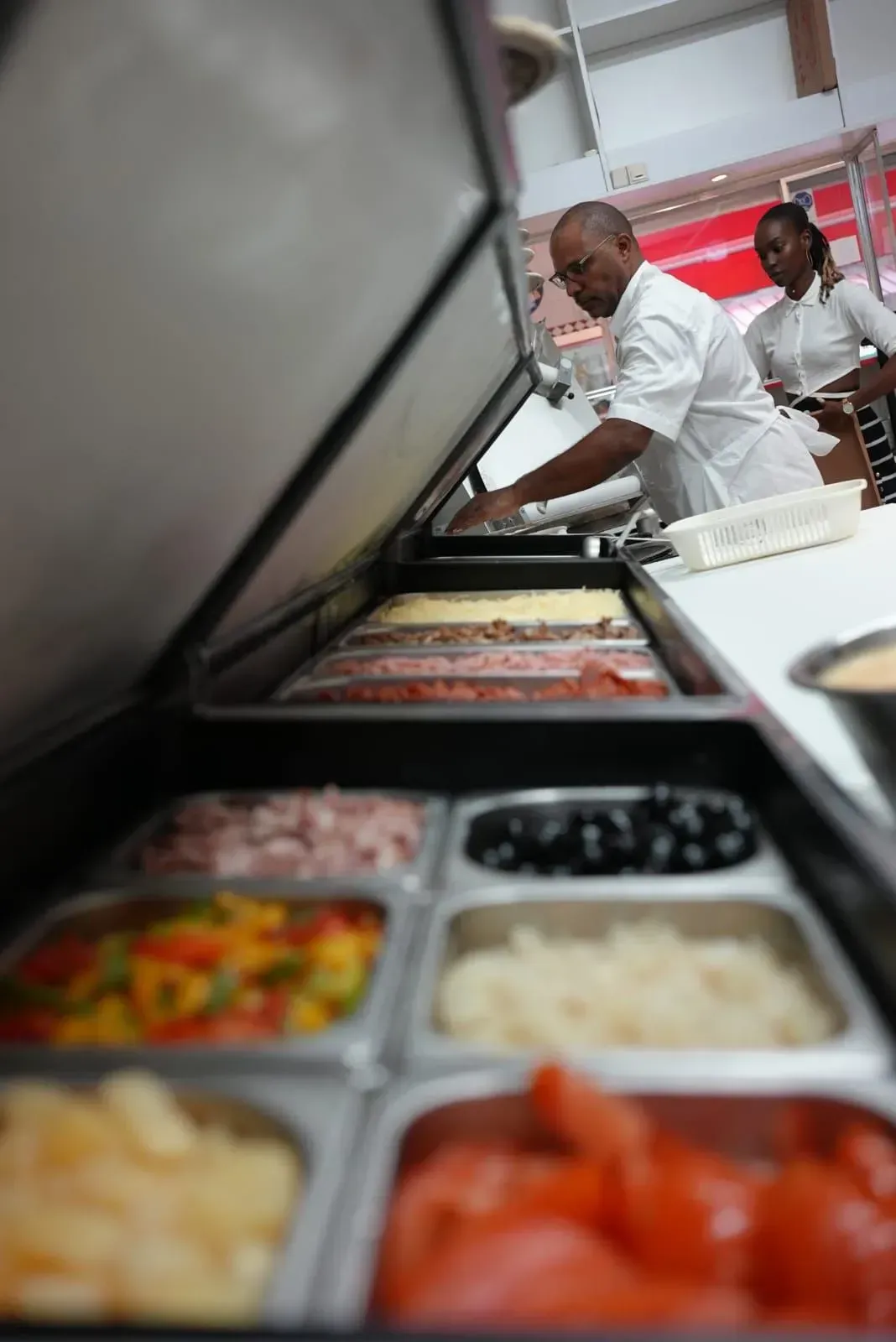 Un buffet avec des plateaux-repas et deux employés servant au comptoir dans une cafétéria
