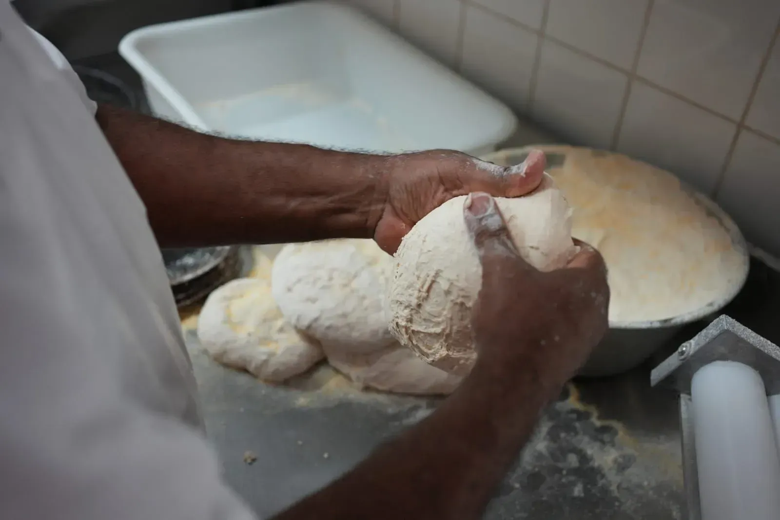 Des mains pétrissent de la pâte sur un plan de travail fariné, à côté d'un saladier, dans une cuisine.