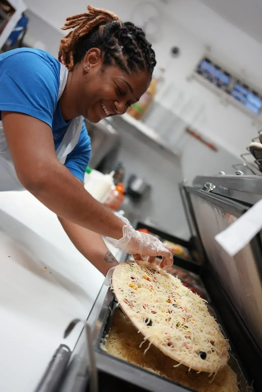 Personne garnissant une grande pizza dans une cuisine commerciale