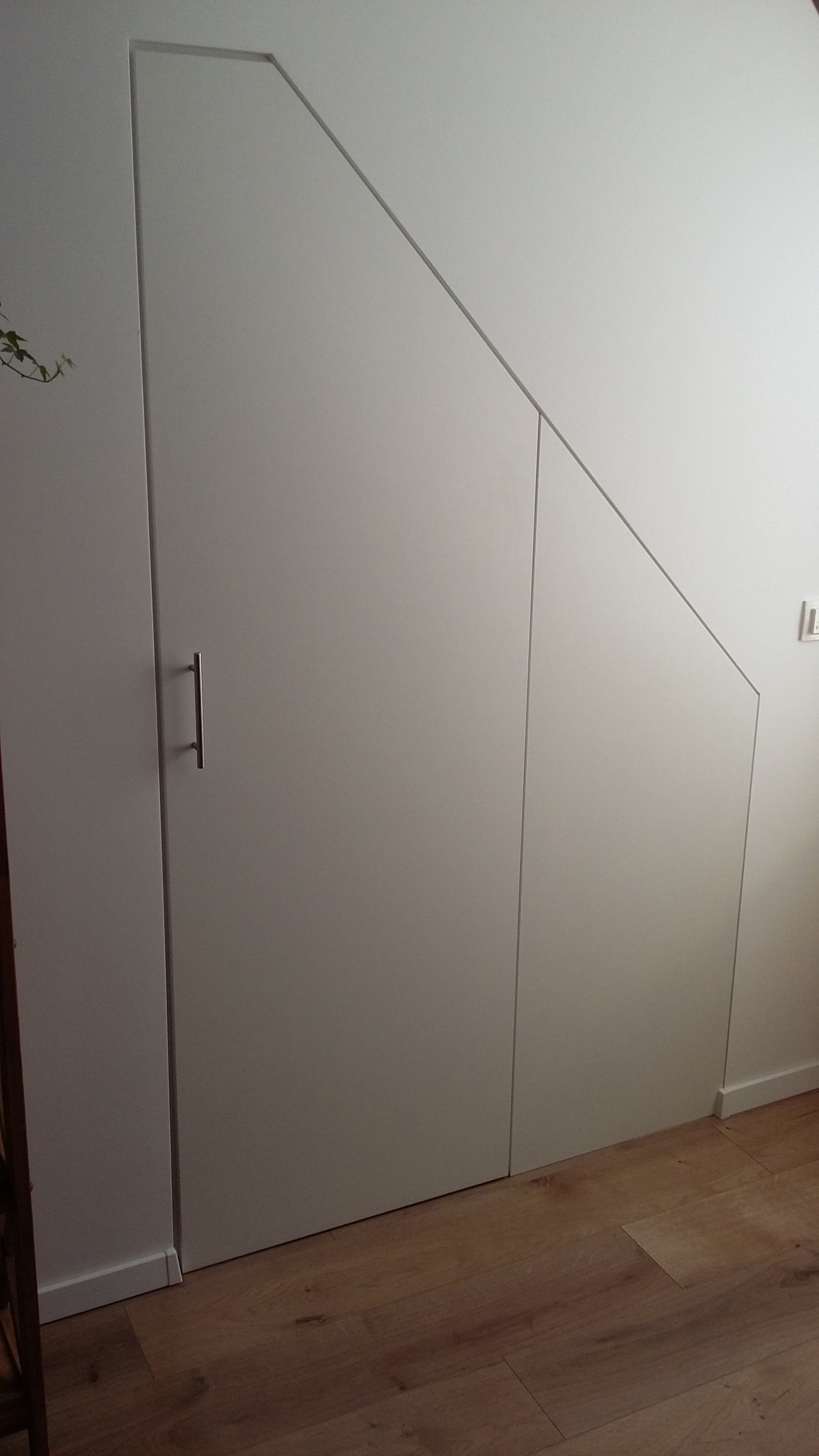 In einem Zimmer befindet sich unter einer Treppe eine weiße Tür.