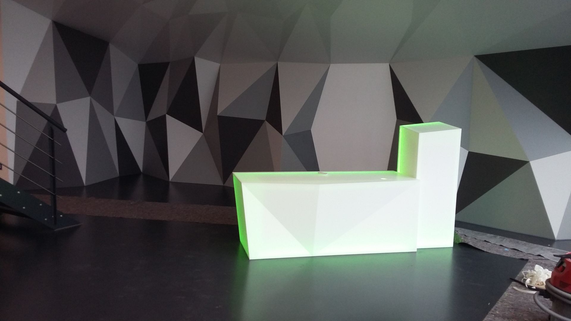 In einem Raum neben einer Treppe steht ein grün beleuchteter Würfel.