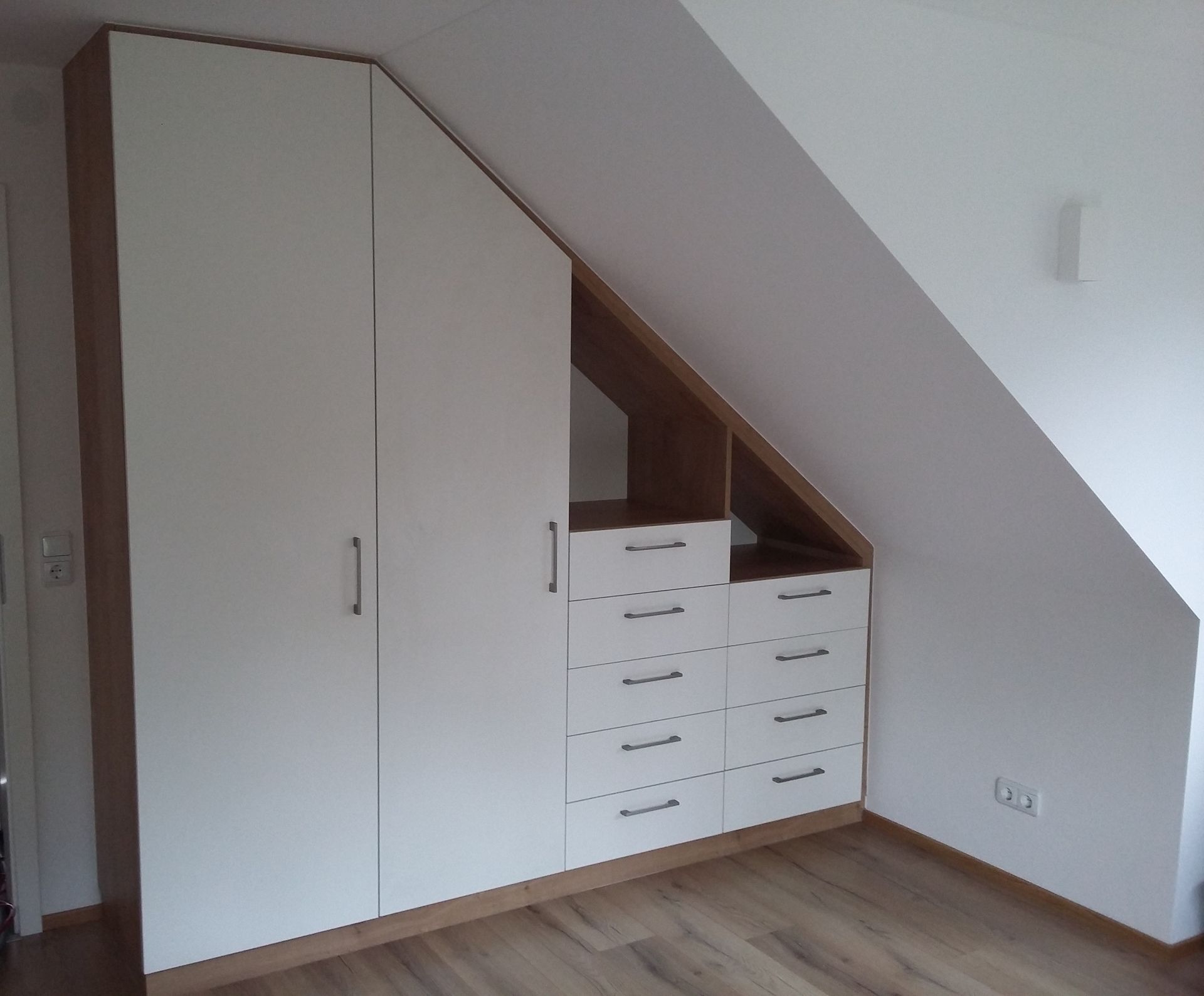 Ein Schlafzimmer mit Dachschräge und darunter einem Kleiderschrank mit Schubladen