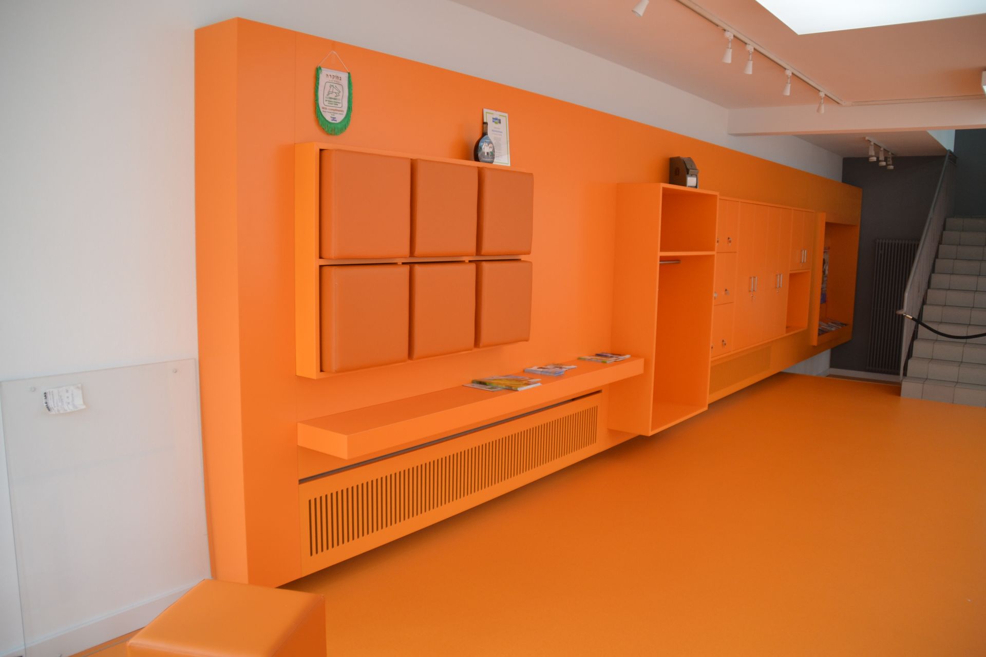 Eine lange orangefarbene Wand mit einem Regal und einer Treppe im Hintergrund.