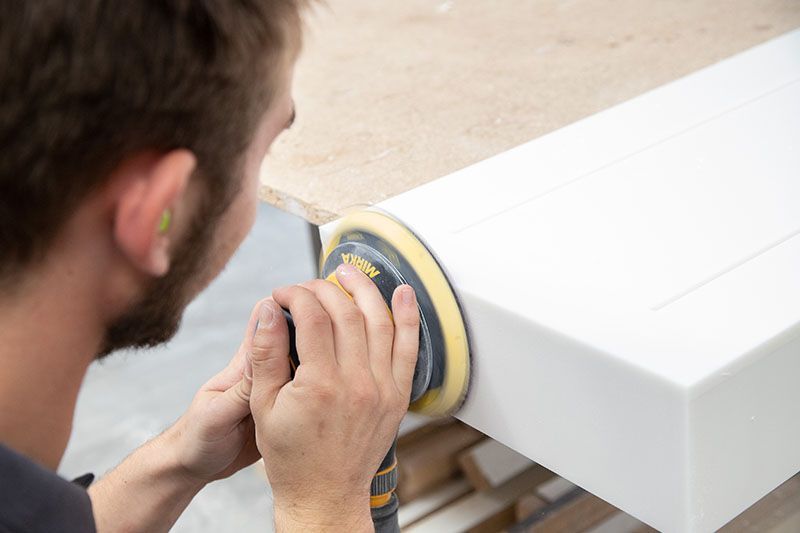 Ein Mann schleift mit einer Schleifmaschine ein Stück Holz.
