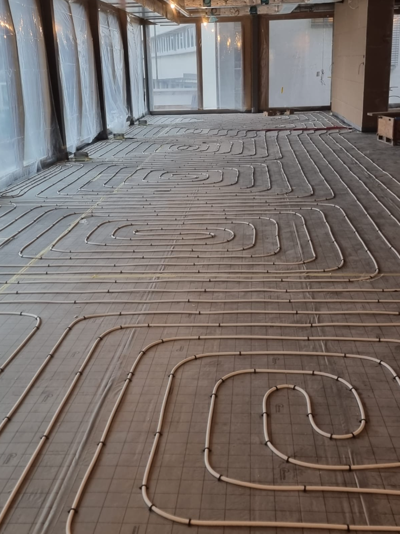 Ein Arbeiter verlegt Laminatboden über Fussbodenheizungsrohren, die auf einem reflektierenden Unterboden verlegt sind.
