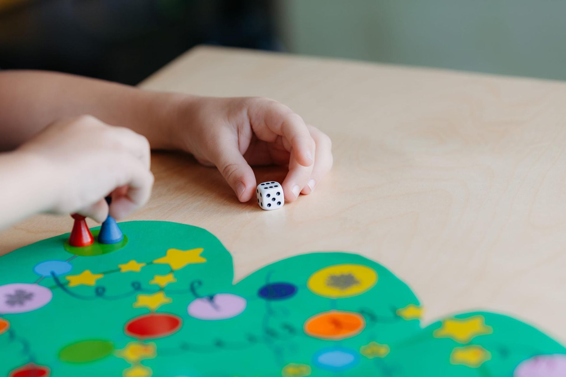 Manos lanzando un dado sobre un tapete de juego de mesa colorido con pequeñas fichas de juego.