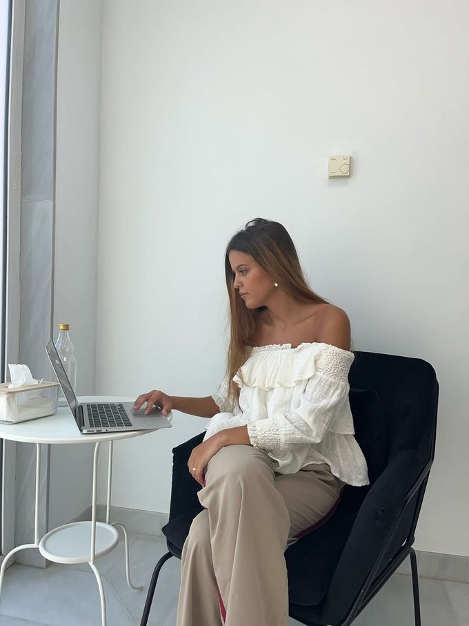 Mujer sentada en una mesa pequeña usando una computadora portátil en una habitación luminosa y minimalista.