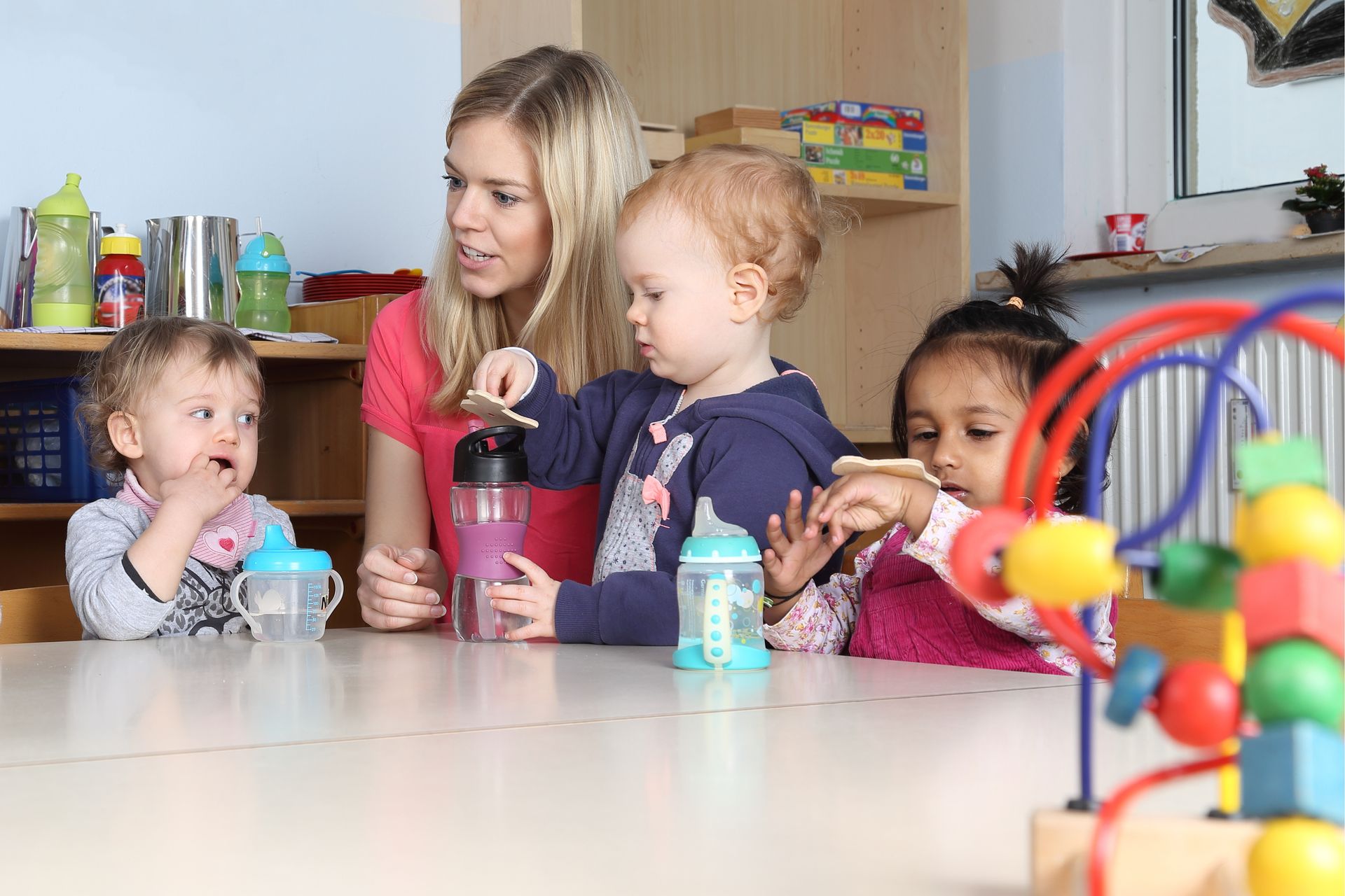 Une jeune femme s'occupe de trois enfants, dont les biberons sont posés sur une table