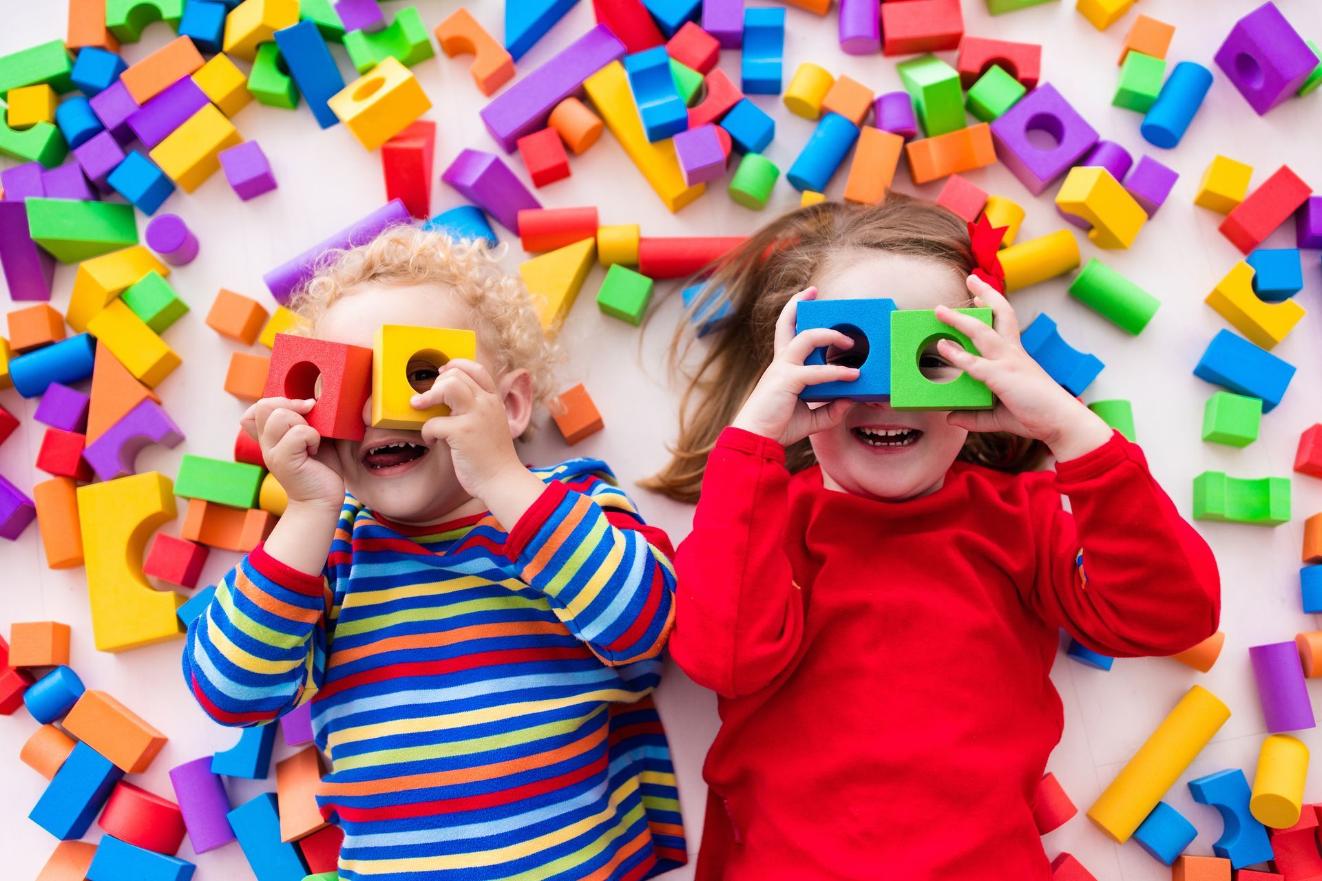 Deux enfants souriants sont couchés au milieu de blocs colorés