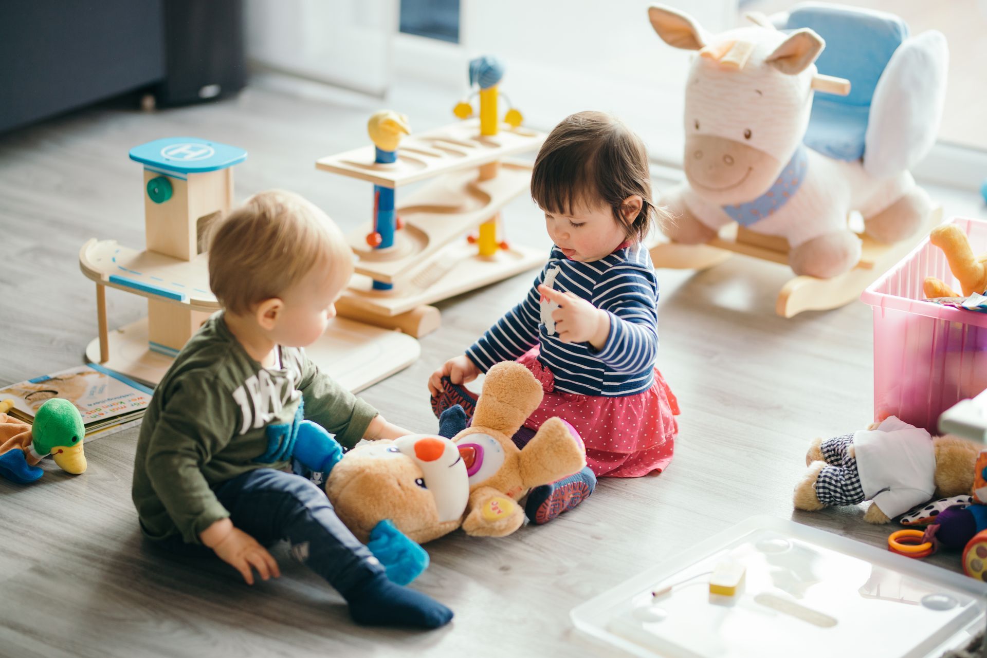Deux tout-petits jouent avec des peluches, entourés de jouets en bois