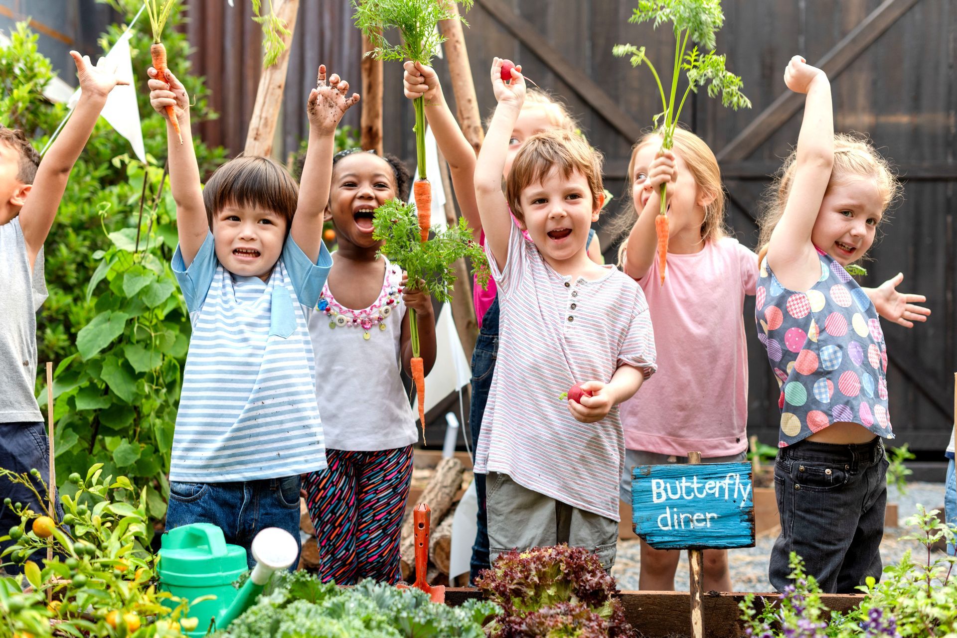 Des enfants, dans un jardin, brandissent des légumes fraîchement cueillis