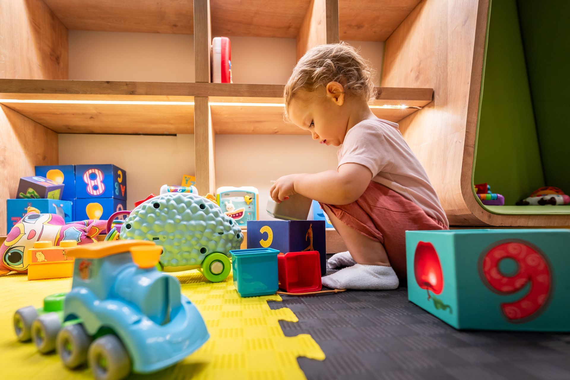 Un enfant joue dans sa chambre avec des cubes de construction, sur un tapis d'éveil jaune et noir