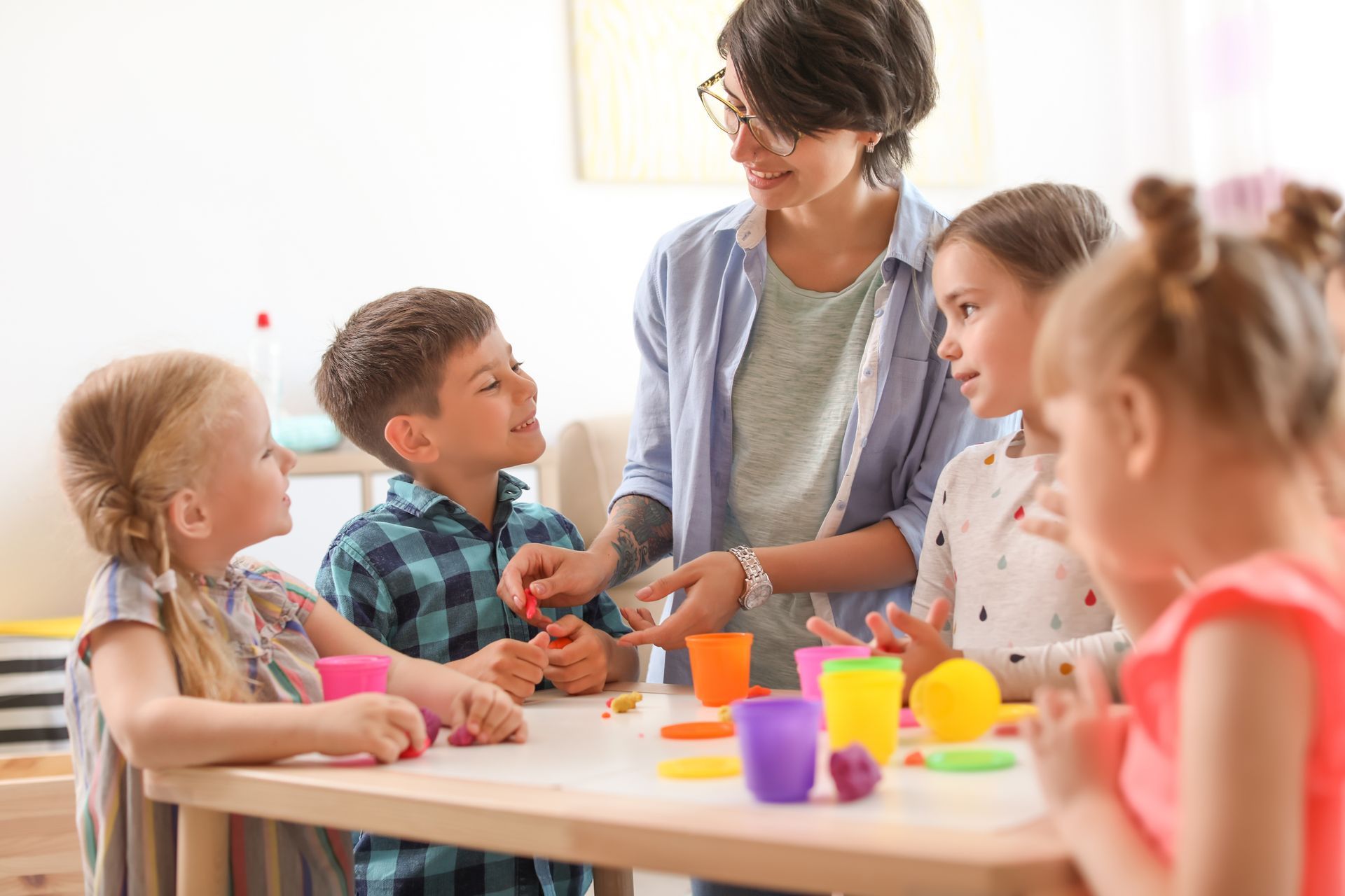 Une jeune femme anime un atelier créatif pour des enfants, avec de la pâte à modeler