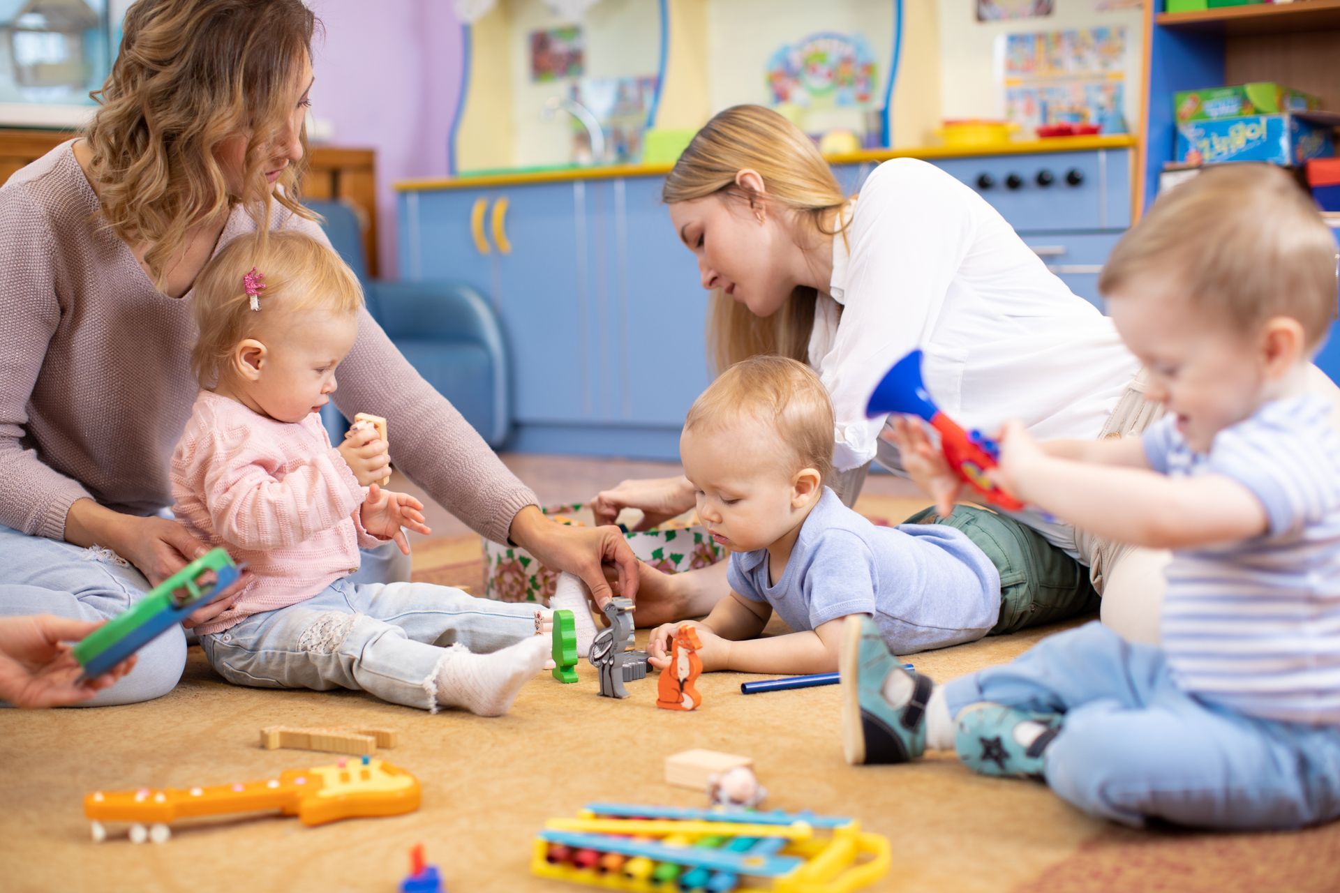Deux éducatrices et trois enfants en bas âge jouent avec des figurines en bois en forme d'animaux