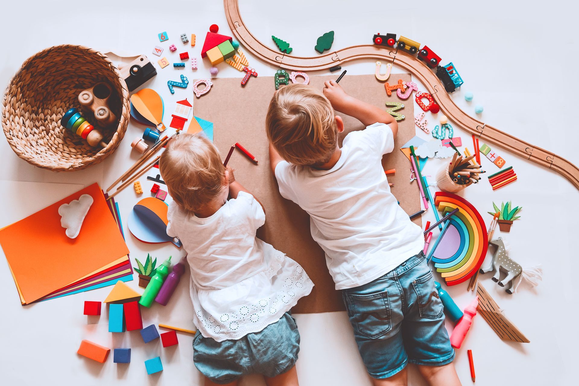 Deux jeunes enfants dessinent sur une grande feuille Canson entourée de jeux éducatifs et de matériel créatif