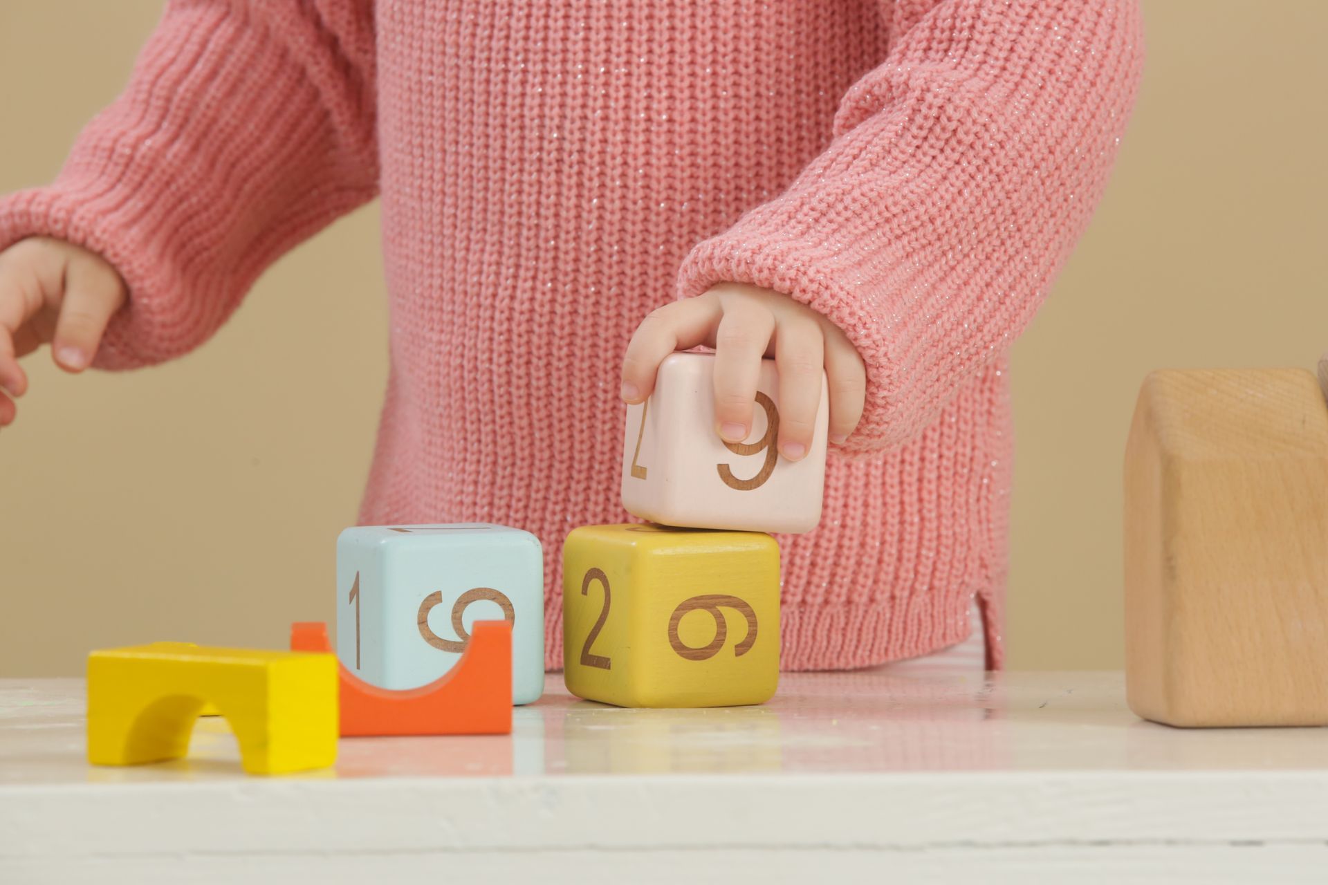 Un enfant en pull rose joue avec des dés en bois