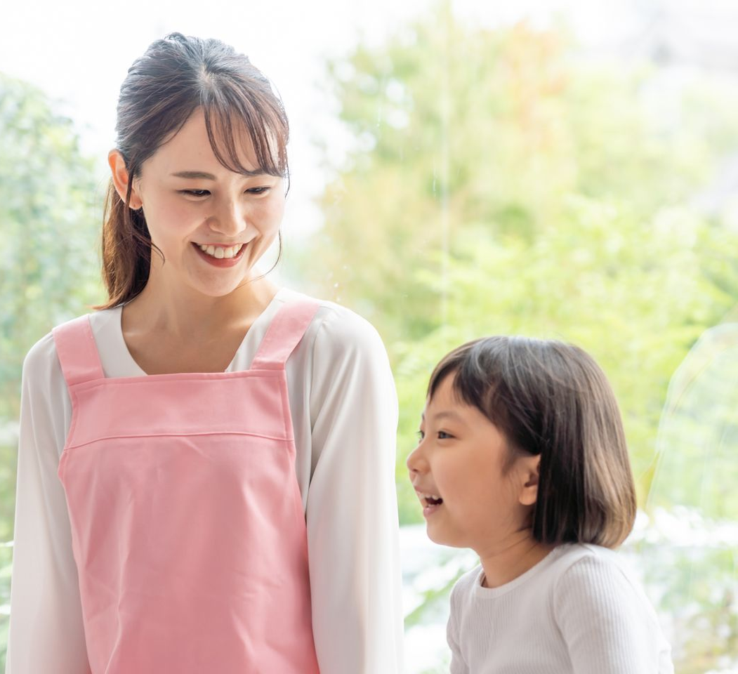 Une femme souriante avec un tablier rose regarde une petite fille