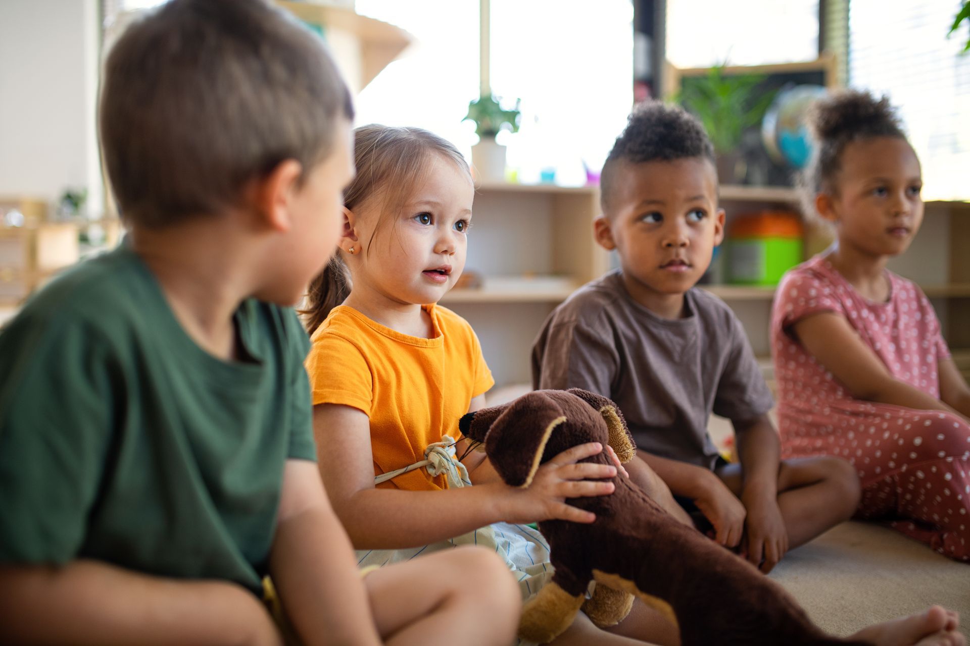 Des enfants assis sur un tapis ; une petite fille tient une peluche en forme chien