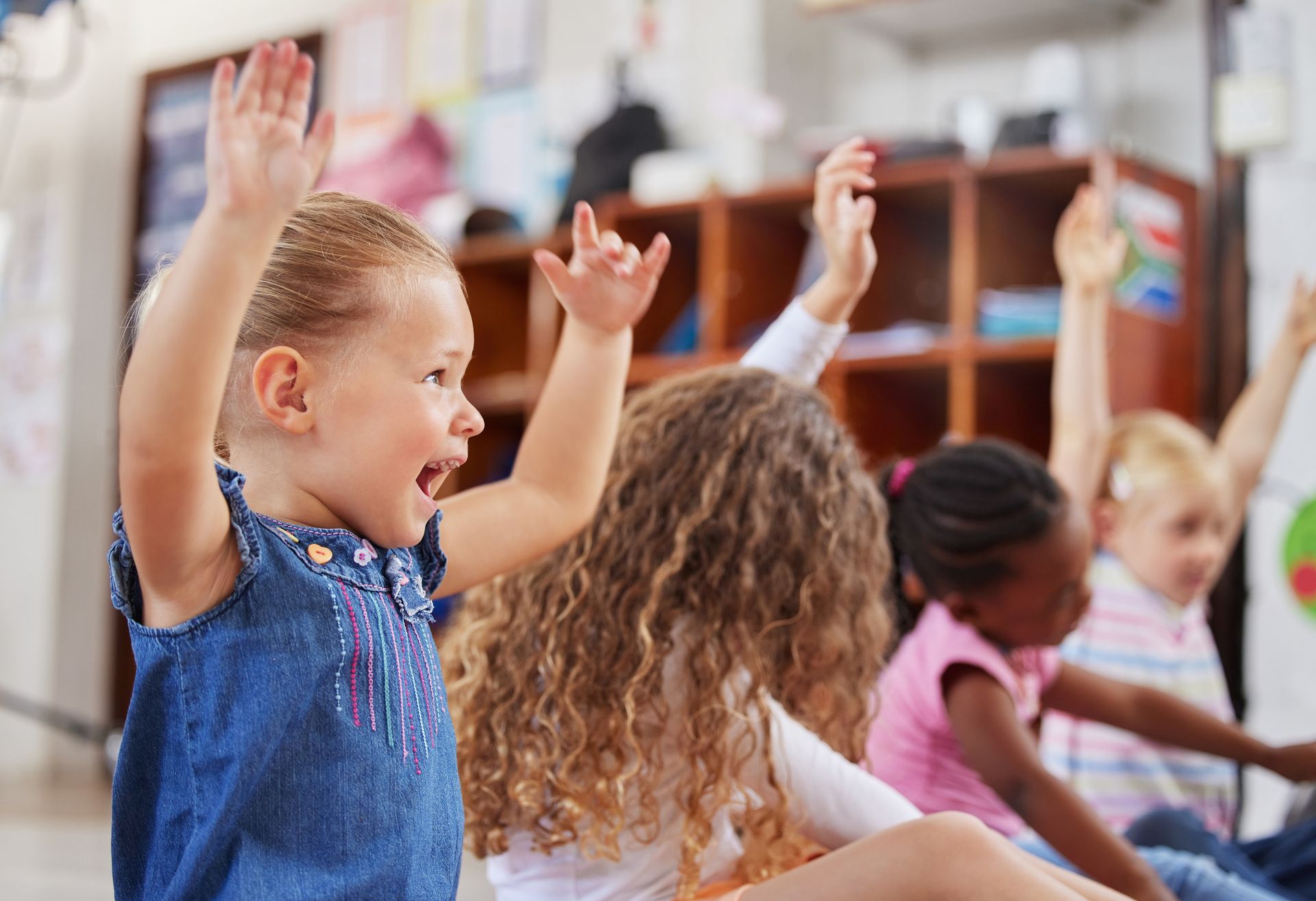 Moment d’échange et d’apprentissage dans une classe maternelle, où des enfants lèvent les mains en souriant