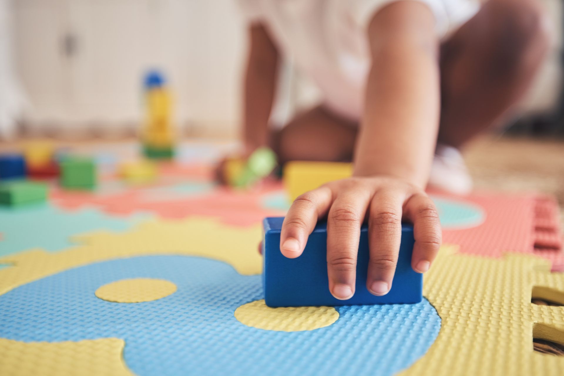Main d'enfant empilant des blocs bleus sur un tapis d'éveil