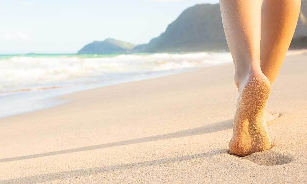 Eine Frau läuft barfuß am Strand.