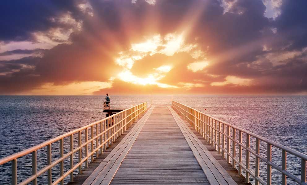 Ein Holzsteg, der bei Sonnenuntergang zum Meer führt.