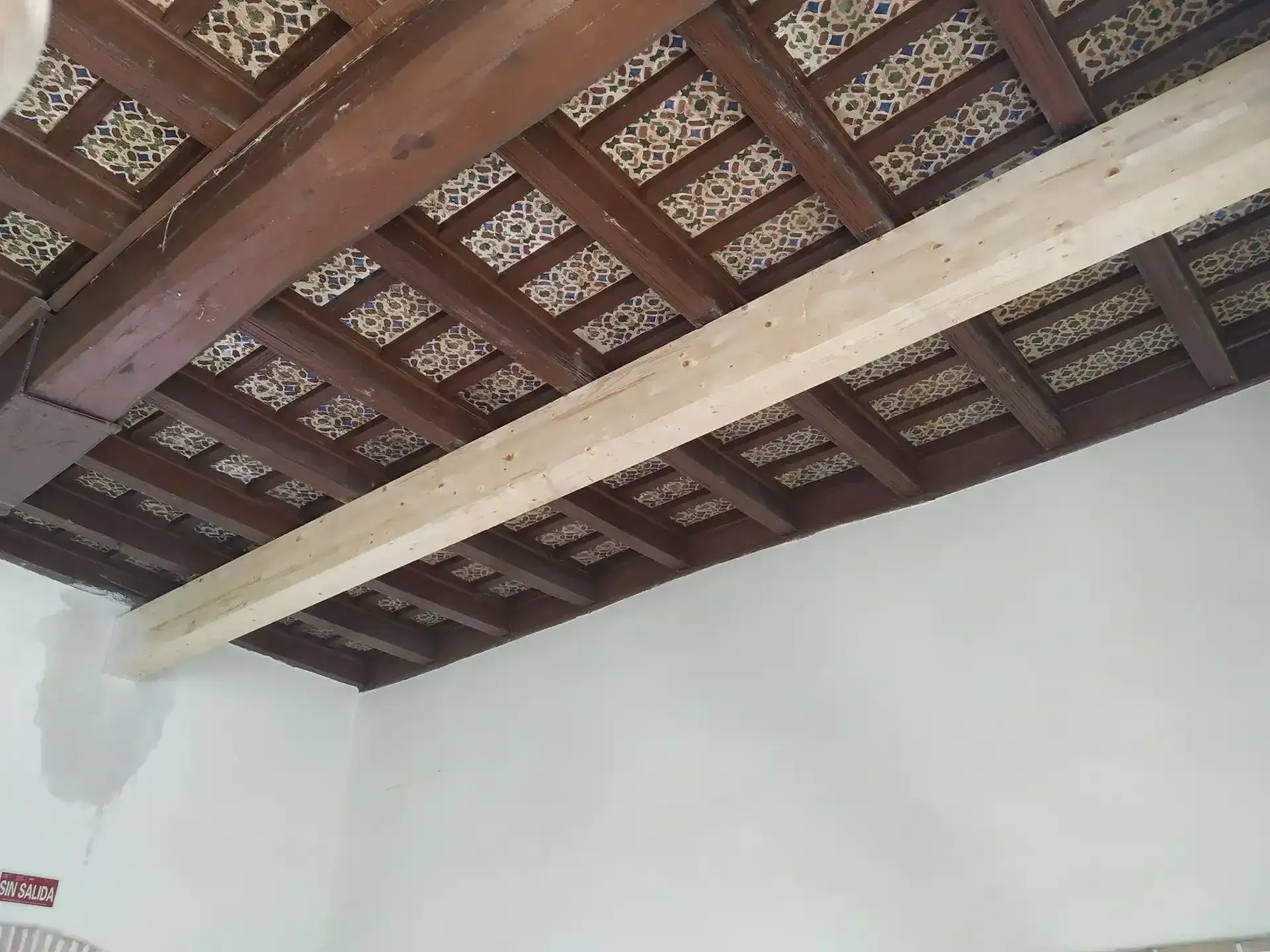 Techo interior con vigas de madera a la vista y tejas de arcilla sobre paredes blancas.