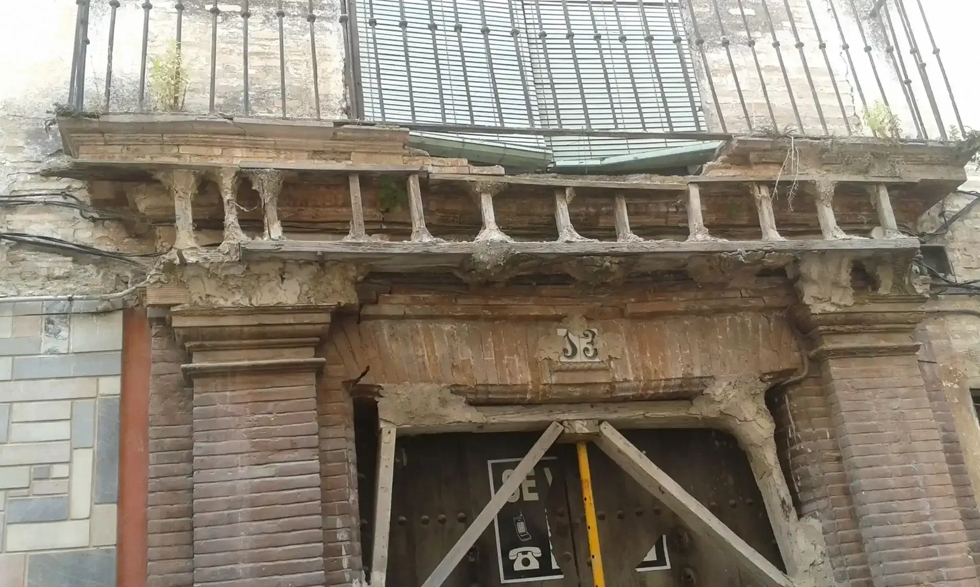 Entrada de un antiguo edificio de ladrillo con andamios y una ventana enrejada sobre la puerta.