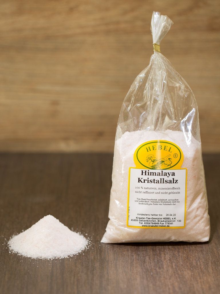 Ein Beutel mit Himalaya-Kristallsalz neben einem kleinen Salzhaufen auf einer Holzfläche