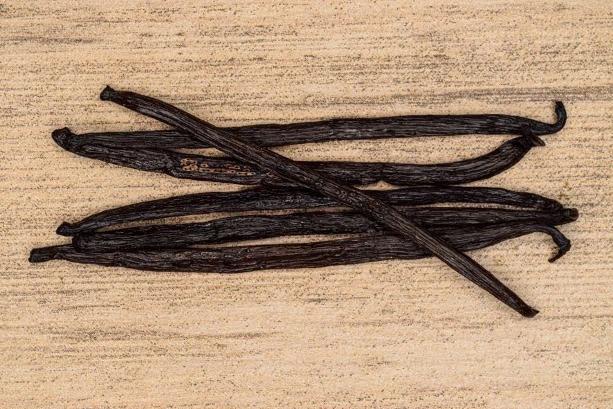 Mehrere dunkle Vanilleschoten auf einer hellen Holzoberfläche