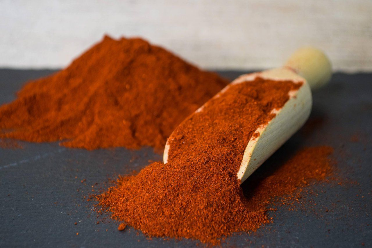 Ein Haufen rot-orangefarbener gemahlener Gewürze neben einer umgekippten Schaufel auf grauer Oberfläche