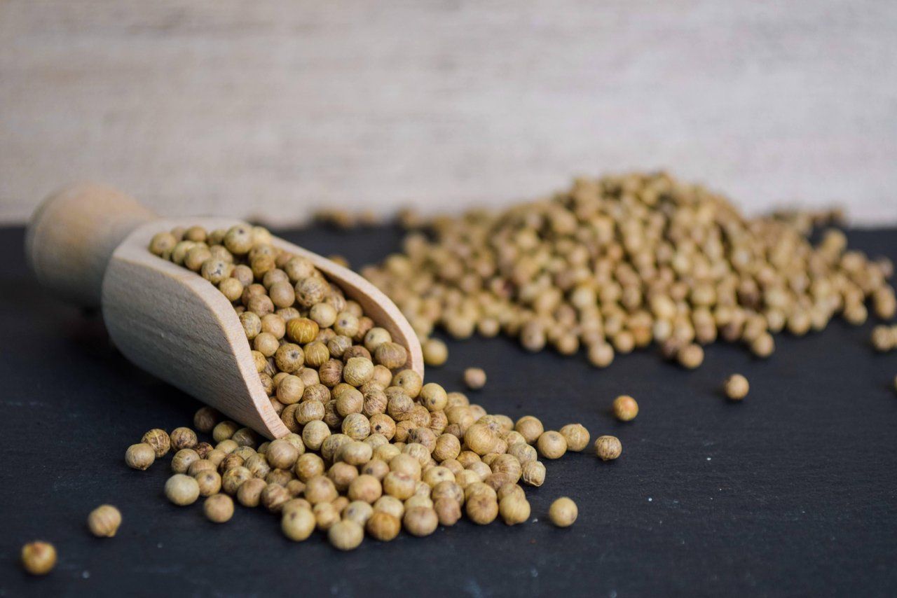 Eine Holzschaufel verschüttet beige Pfefferkörner auf eine dunkle Oberfläche.