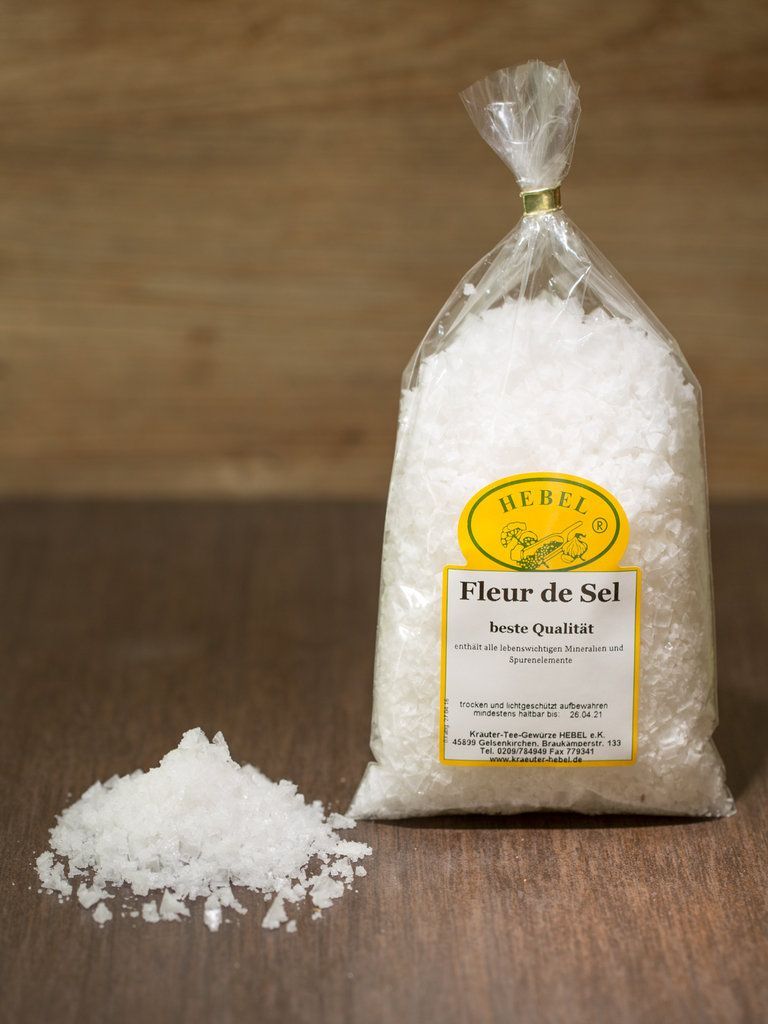 Beutel mit Fleur de Sel Meersalz, auf dem grobes weißes Salz verschüttet wurde, auf einer Holzoberfläche