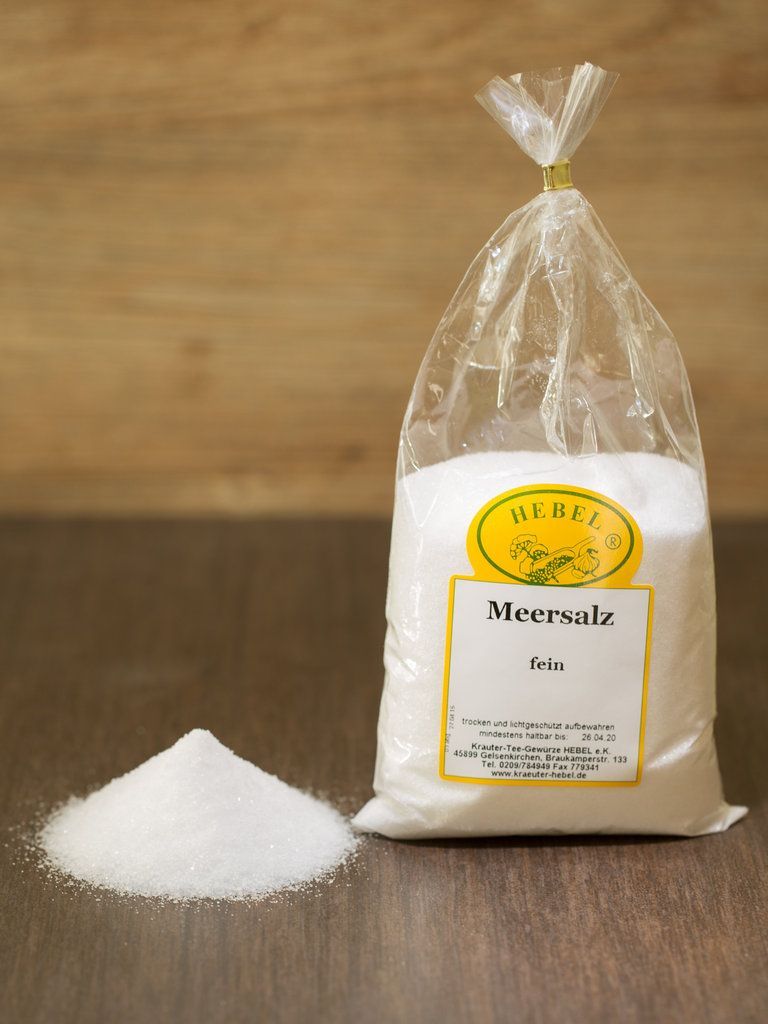 Ein Beutel Speisesalz neben einem kleinen weißen Salzhaufen auf einer Holzfläche.