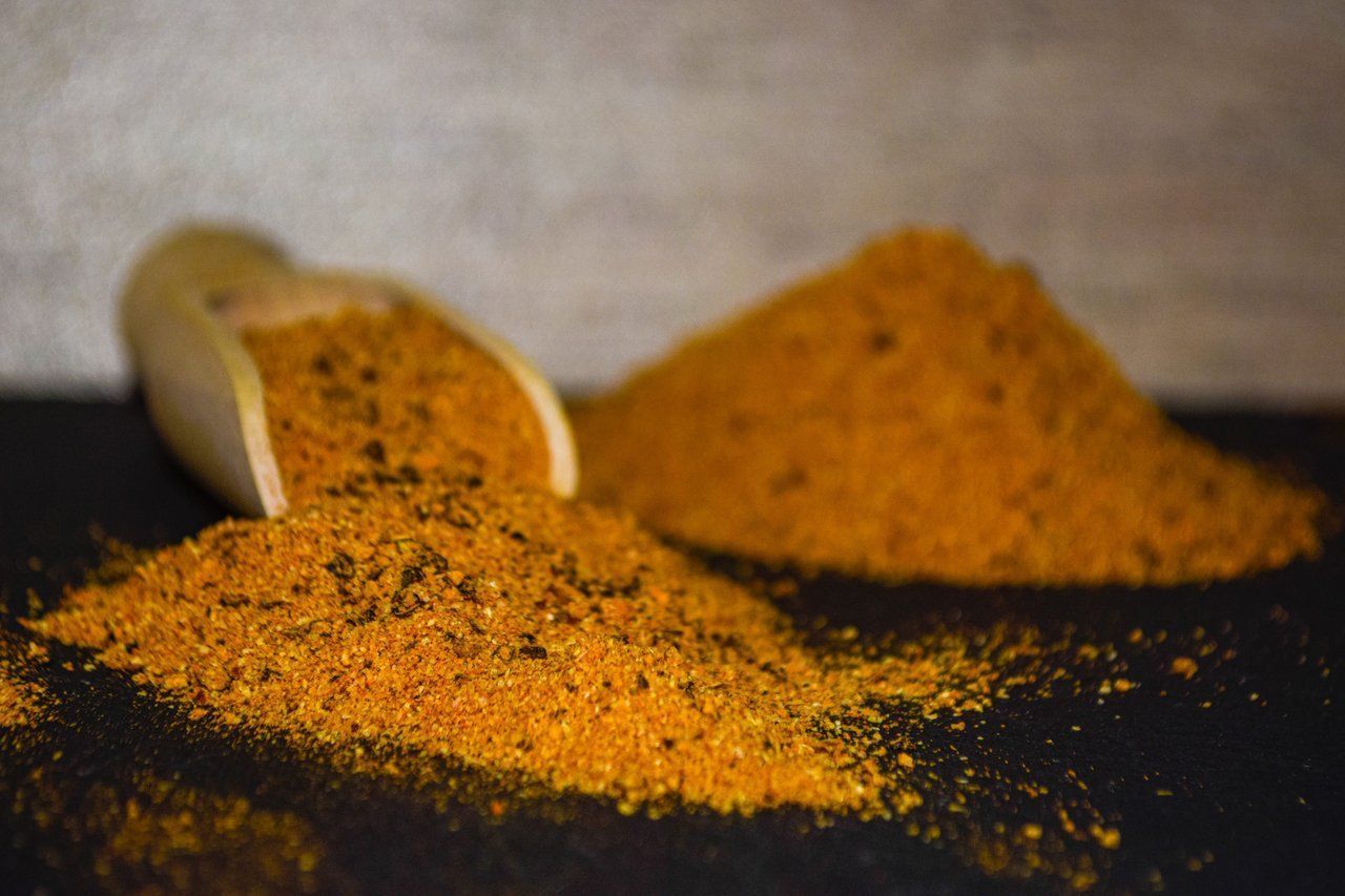Ein Holzlöffel verschüttet goldene Gewürze auf eine dunkle Oberfläche, daneben ein kleiner Haufen.