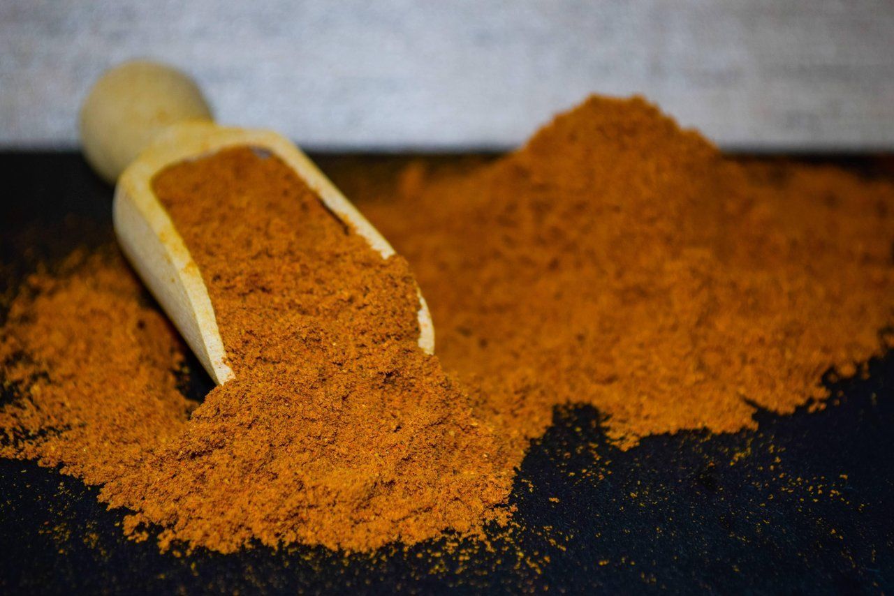 Eine Holzschaufel verschüttet orangebraune Gewürze auf eine dunkle Oberfläche.