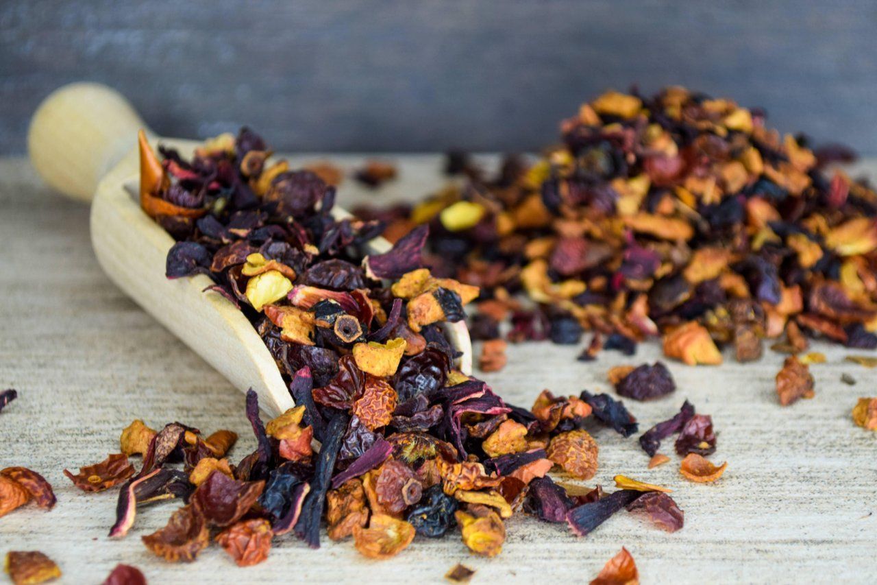 Eine Holzschaufel verschüttet Trockenfrüchte und Teeblätter auf eine rustikale Oberfläche.