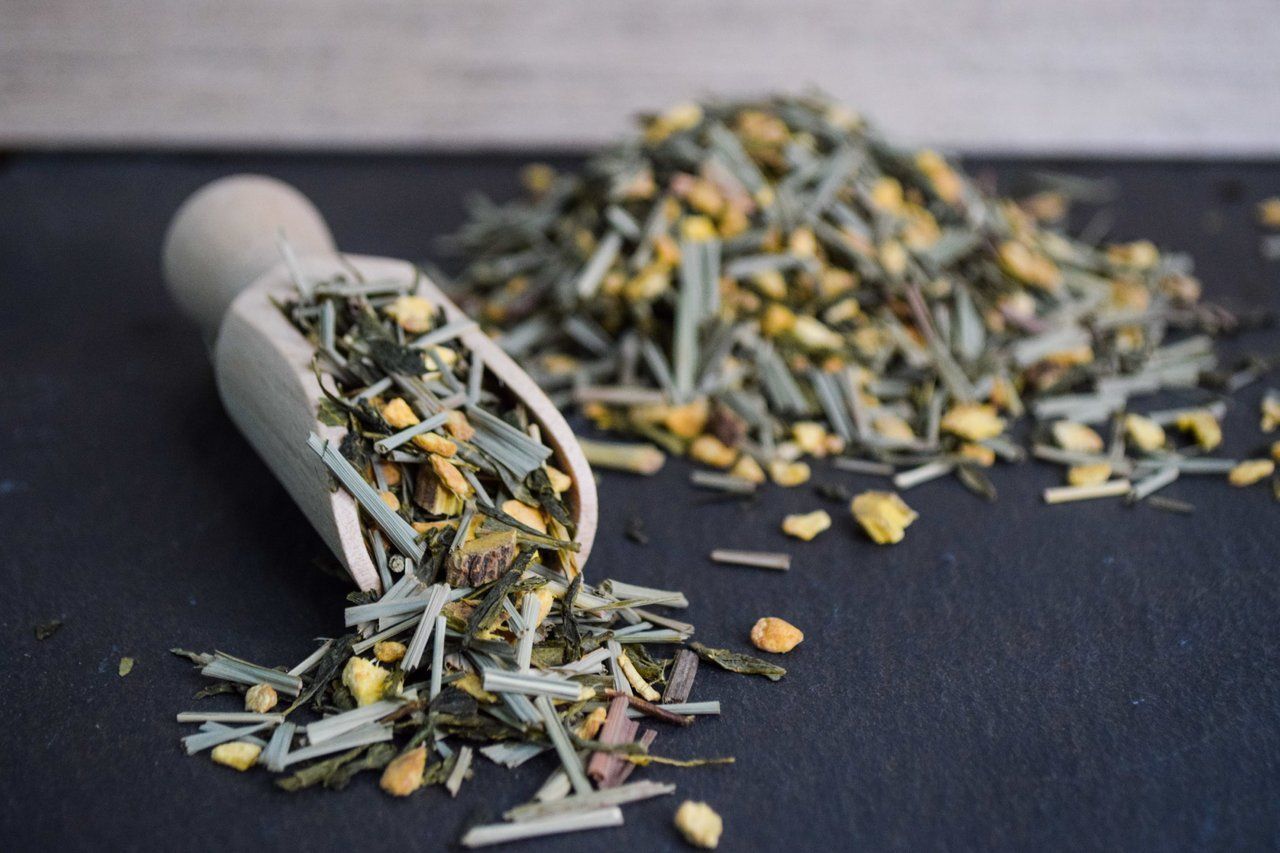 Verschüttete lose Teeblätter aus einem umgekippten weißen Löffel auf einer dunklen Oberfläche